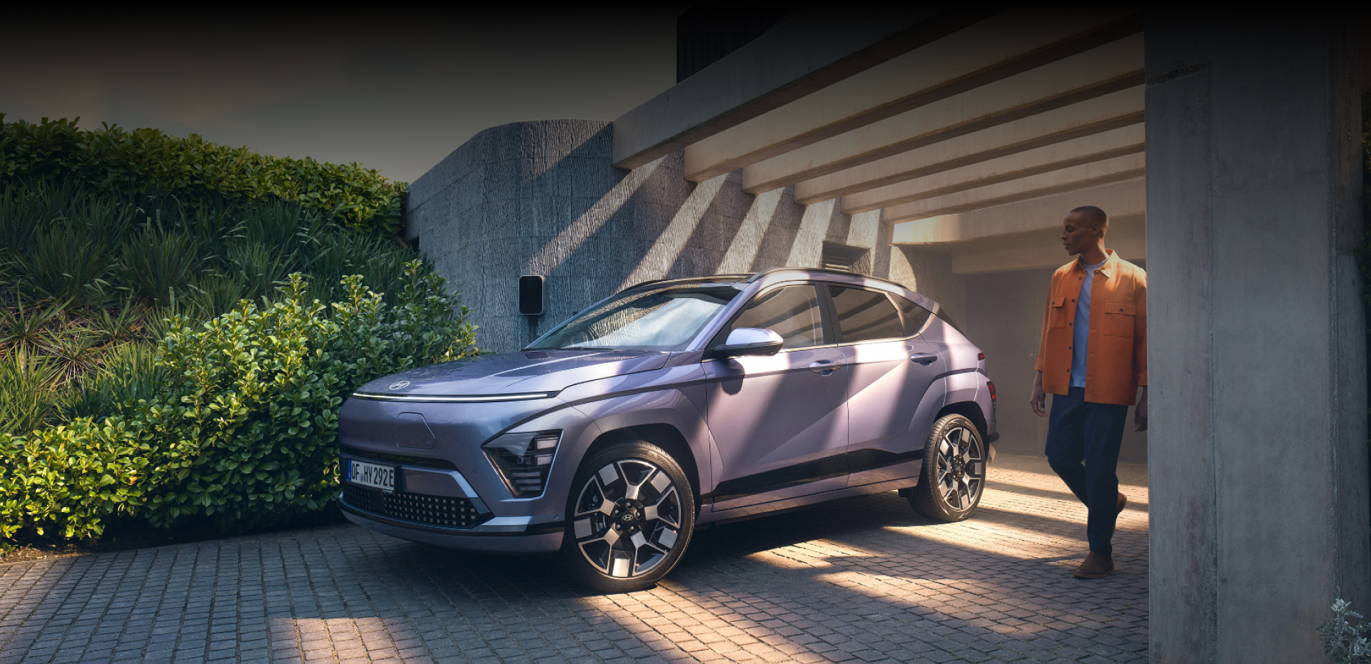 The Hyundai KONA Electric bathed in sunlight with a man walking away from a garage.